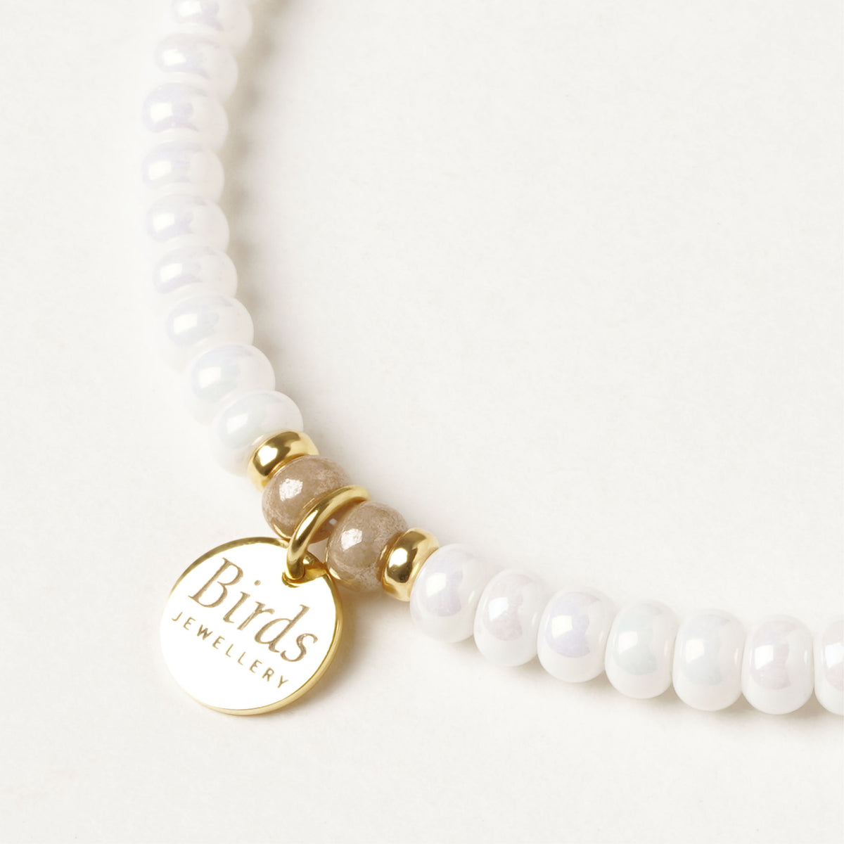 Detalhe da medalha em prata 925 dourada da pulseira Branco & Bege Vidrado Birds Jewellery.
